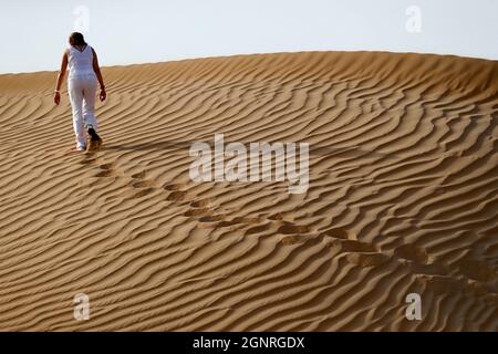 Woman leaving footprints and going up desert sand dune.   Dubai. United Arab Emirates. Stock Photo