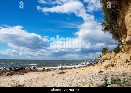 Steep coast with sandy beach and boulders on the Baltic Sea on a summer day with blue sky and clouds Stock Photo