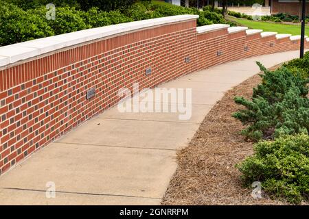 Curved descending sidewalk ramp flanked on one side with a clean, well maintained brick retaining wall, neat bushes and landscaping, horizontal aspect Stock Photo