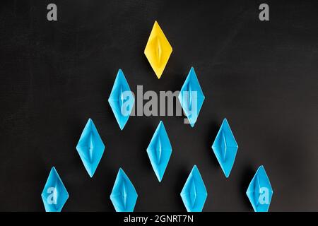 Leadership concept. Group of paper boat on blackboard background. One leader ship leads others Stock Photo