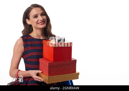 Portrait of smiling young Caucasian woman standing with stack of gift boxes against isolated background Stock Photo