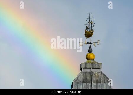 Weymouth, Dorset, UK.  27th September 2021. UK Weather.  A rainbow arches up into the sky above a weather vane in the shape of a ship on top of the Morrisons supermarket at Weymouth in Dorset as the sun comes out after a heavy rain shower.  Picture Credit: Graham Hunt/Alamy Live News Stock Photo