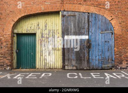 Keep Clear sign in front of wooden doors that have peeling paint and brick surround. Hereford UK. June 2021 Stock Photo