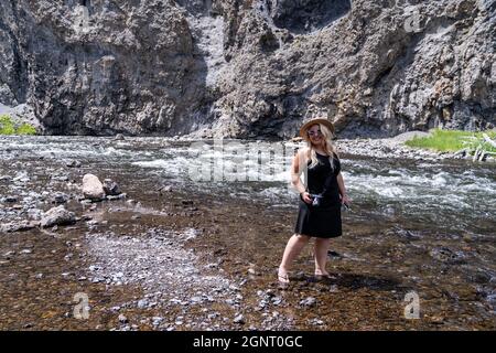 Cute blonde tourist woman dipping her feet in the Firehole River in Yellowstone National Park Stock Photo