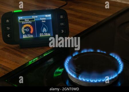 Smart meter readings of gas and electricity usage on a home smart energy monitor next to cooker with gas hob flame Stock Photo