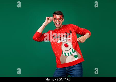 Photo portrait man wearing funny glasses dancing xmas party showing ugly sweater isolated green color background Stock Photo