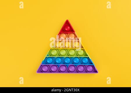 Bright rainbow toy antistress for children and adults on a yellow background. Flexible sensory antistress toy pop it triangle shape Stock Photo