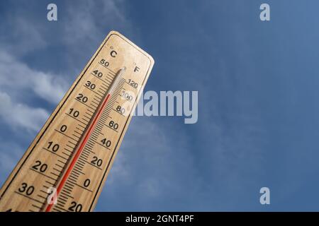 Wooden thermometer with red measuring liquid showing high temperature over 32 degrees Celsius on background of blue sky with clouds. Concept of heat w Stock Photo