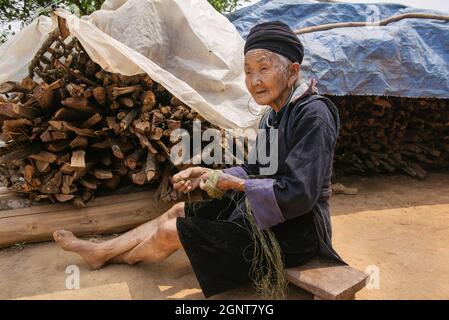 Sapa, Vietnam - April 14, 2016: Old vietnamese woman in the village near Sapa doing handmade thread of hemp. Black Hmong minority women in traditional Stock Photo