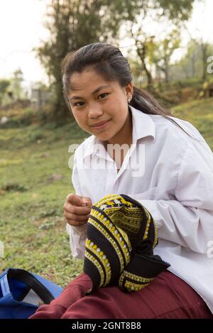 Sapa, Vietnam - April 14, 2016: Young vietnamese girl in the village near Sapa doing handmade. Black Hmong minority female stitch outdoors. Stock Photo