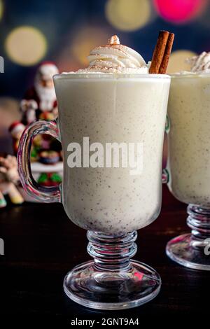 Mugs of Eggnog Topped with Whipped Cream and Cinnamon with a Christmas Setting: Footed mugs of homemade eggnog garnished with whipped cream Stock Photo