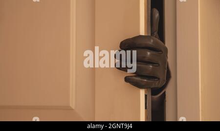Housebreaking, burglary concept. Gloved hand opening the entrance door, burglar entering illegally the house Stock Photo
