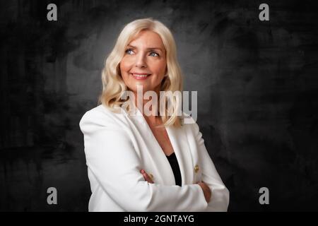 Studio portrait smiling grey haired senior woman standing at isolated dark grey  background. Copy space. Stock Photo