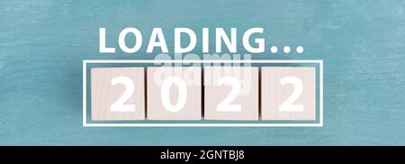 The year 2022 is standing in white letters on wooden cubes, the word loading is standing above Stock Photo
