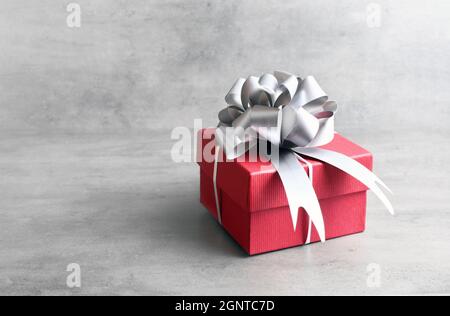 Single red gift box with silver ribbon on grey background. Stock Photo