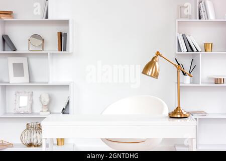 Modern fashionable freelance workplace with table, lamp, bookshelves. Minimalist style freelancer desk in white, remote work and home office concept Stock Photo
