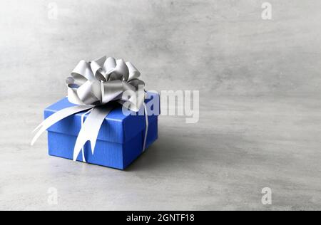 Single blue gift box with silver ribbon on grey background. Stock Photo