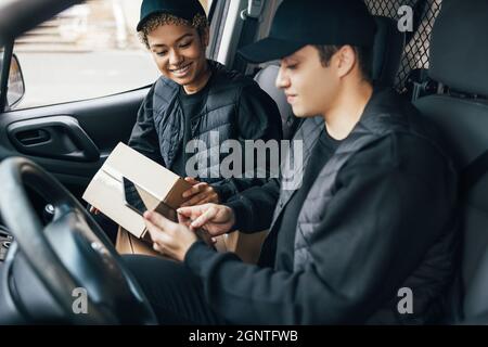 Two couriers in uniform sitting in a van checking delivery information on a digital tablet Stock Photo