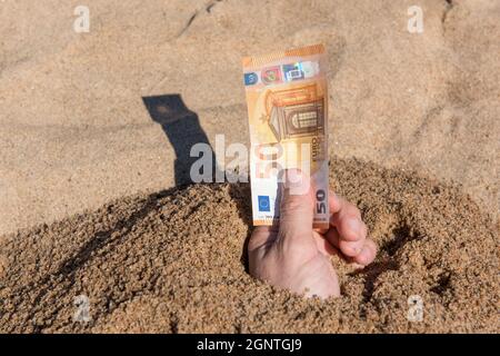 Fifty euros in the hand of a man sticking out of the sand Stock Photo