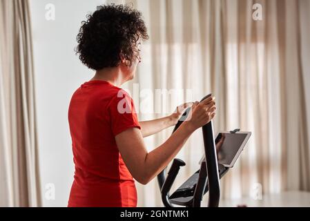 Woman exercising at home with online cross training elliptical class Stock Photo