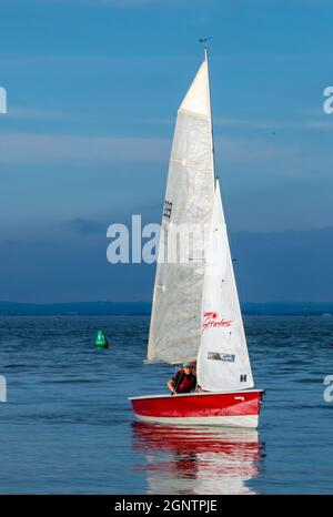 sailing dinghy on flat calm sea in the atmospheric evening light. small sailing boat off of the coast of the isle of wight in light airs calm day Stock Photo