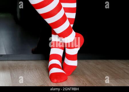 Female legs in Christmas knee socks on a floor on black wardrobe background. Clothing for New Year celebration, girl in Santa costume