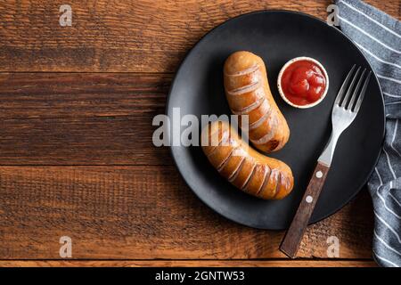 Grilled sausages with tomato sauce on plate on a wooden table background, top view copy space Stock Photo