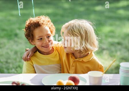 Portrait of two smiling boys embracing at picnic table outdoors while enjoying Birthday party in Summer, copy space Stock Photo