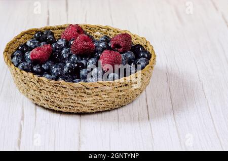 Fresh blueberries and raspberries in a small wicker basket. Stock Photo