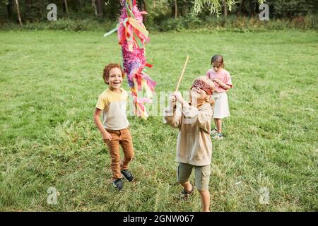 High angle portrait of boy playing pinata game at Birthday party outdoors and holding bat, copy space Stock Photo