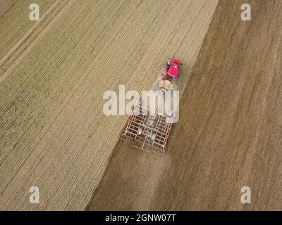 Aerial photo of a tractor ploughing stubble field in countryside. Agricultural tractor plows soil field for sowing. Aerial top view from the drone . Stock Photo