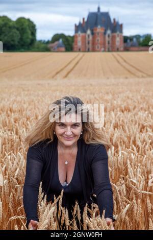 a blonde mature women traveler in a field of wheat ears in front of a Renaissance castle. Stock Photo