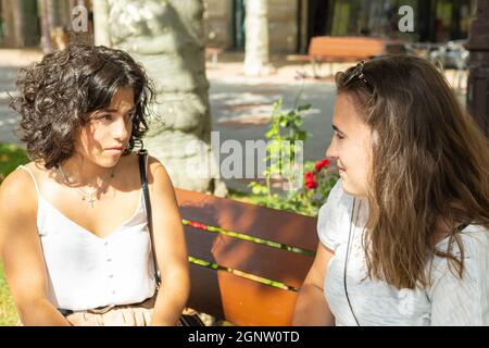 two college students talking while sitting on a bench on campus Stock Photo