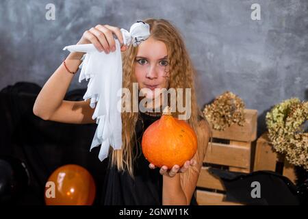 Shaggy teenage girl among decor in black and orange tones for Halloween holiday with ghost in hand Stock Photo