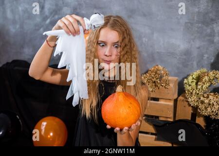 Shaggy teenage girl among decor in black and orange tones for Halloween holiday with ghost in hands Stock Photo