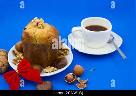 Still life of a table with a panettone decorated with nuts next to a cup of coffee on a blue background to celebrate Christmas Stock Photo