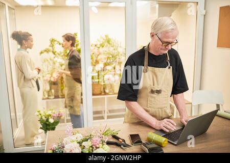 Portrait of male small business owner using laptop and wearing mask while managing flower shop, copy space Stock Photo