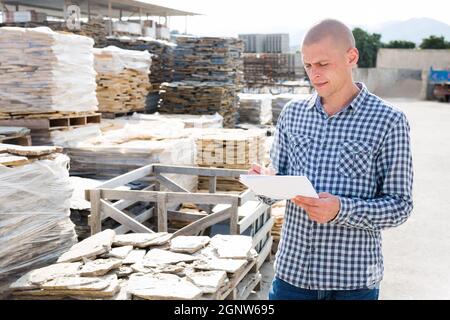 Man worker with papers collecting order at warehouse Stock Photo