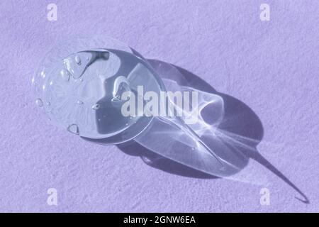 Single blob of transparent glycerin or gel smear smudge swatch on lilac backdrop with shadow. Glossy texture with tiny bubbles. Styling gel lotion Stock Photo