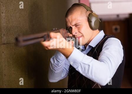 Concentrated man practicing shotgun shooting at firing range Stock Photo