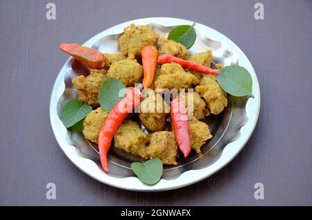 closeup the bunch yellow brown bengal gram fried food with red chilly and green mint in the steel plate over out of focus grey brown background. Stock Photo