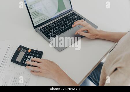 Unrecognizable woman sits at desk with laptop computer calculator papers calculates montly expenses Stock Photo