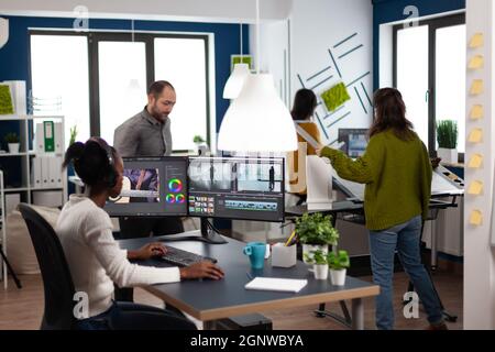 African american video editor wearing headset editing movie using post production software working in start up company office. Black creator processing video footage on computer with dual displays Stock Photo
