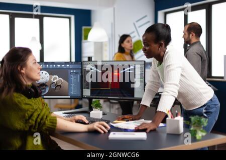 Multiethnic women designer looking at computer with dual displays working together at gaming project in company office. Gamer workers developing new games application on pc with modern technology Stock Photo