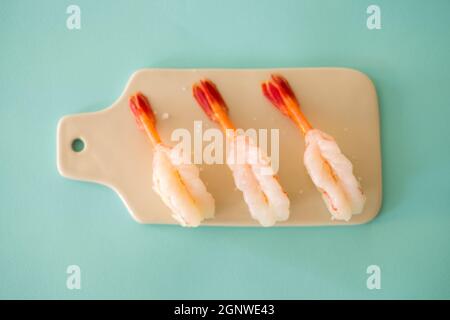 Prawn sushi in japanese restaurant. Sushi - ama Ebi Nigiri on creamy board isolated on turquoise background. Shrimp sushi. High quality photo  Stock Photo