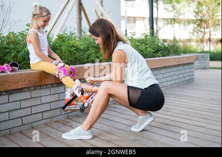 Caucasian woman helping her daughter put on roller skates. Stock Photo