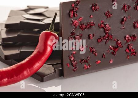 Dark raw chocolate with pepper and freeze-dried cherries on a white background. Stock Photo