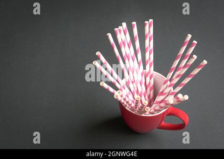 Pink stripe paper straws inside a red cup, on black background. Copy space. Stock Photo