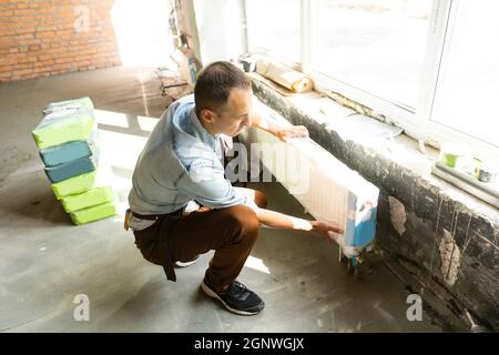 Full length shot of professional plumber, worker in uniform fixing or installing heating radiator. Construction, maintenance and repair concept Stock Photo