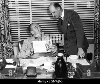FRITZ LANG in his Office at Columbia Studios in February 1953 at the time he was making THE BIG HEAT with LARRY COURTNEY showing him a programme for Spring 1953 Film Classics presumably including a Fritz Lang film Stock Photo